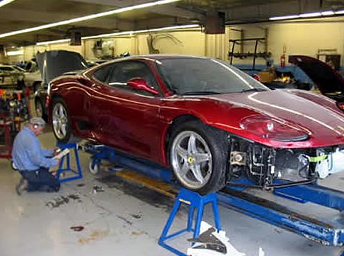 Step 2: Technician kneeling beside the red Ferrari mounted on a blue frame-straightening machine, front bumper removed